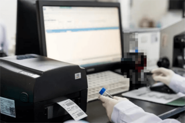 A person operating a バーコードプリンター connected to a computer in a clean workspace.